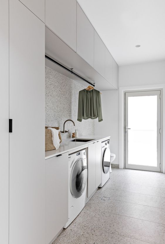 a minimalist dove grey laundry with sleek cabinets, a terrazzo backsplash and a floor, a black faucet and a glass door to the garden