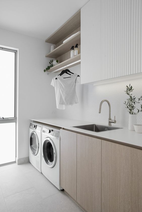 a minimalist neutral laundry with stained and white cabinets, a white penny tile backsplash and white appliances, built-in lights