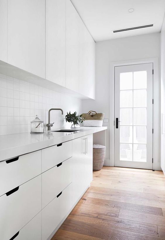 a modern Scandinavian laundry with sleek white cabinets, white square tiles and drawers and a cabinet plus a French door that invites light in