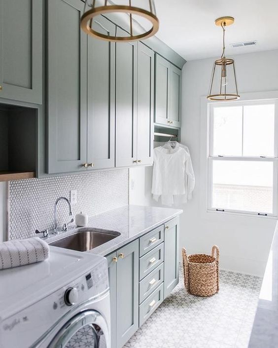 a modern farmhouse laundry with green shaker style cabinets, a penny tile backsplash, a grey and white tile floor