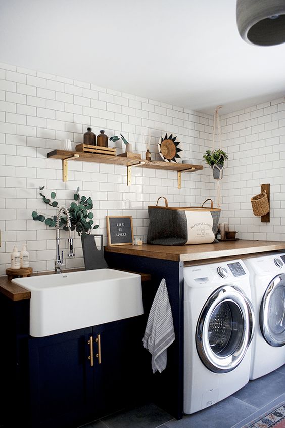 a modern farmhouse laundry with navy cabinets, wooden countertops and open shelving, potted greenery and baskets