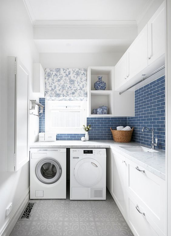 a modern farmhouse laundry with shaker style cabinets, stone countertops, a washing machine and a dryer, blue subway tiles and a floral curtain