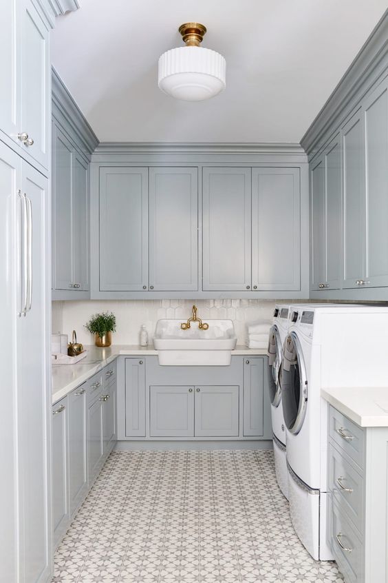 a modern grey laundry with shaker style cabinets, printed tiles on the floor, white coutnertops, a sink with a vitnage faucet and a washing machine and a dryer