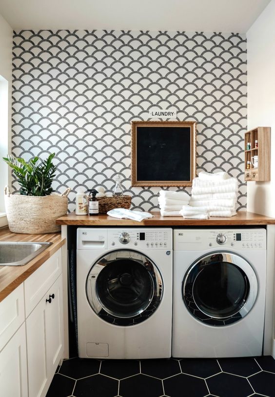 a modern laundry with a scallop accent wall, shaker style cabinets, a washing machine and a dryer, wooden countertops, a small shelf