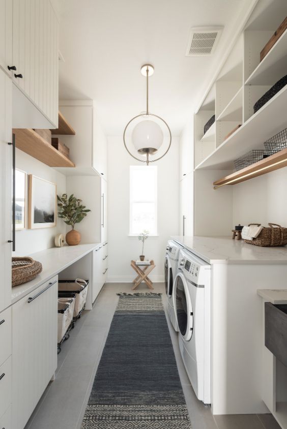 a modern neutral laundry with planked cabinets, open shelves, a console table and baskets, stained shelves and a washing machine and a dryer