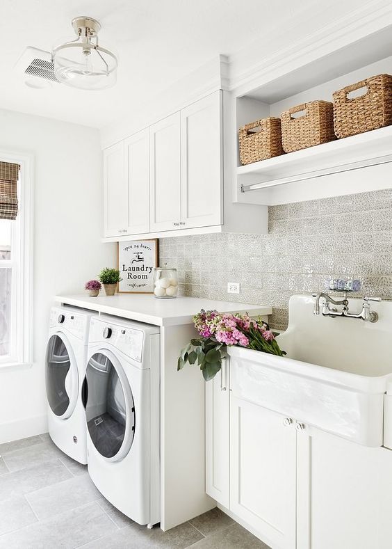 a modern neutral laundry with white shaker cabinets, a large sink, a vintage faucet, baskets for storage and a washing machine and a dryer
