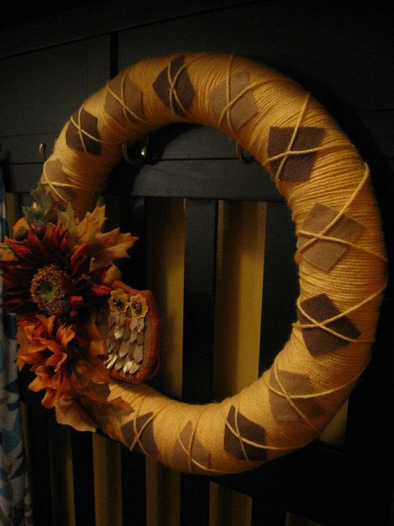 a moody fall wreath covered with orange yarn, brown fabric rhombs and faux blooms and leaves plus a play owl
