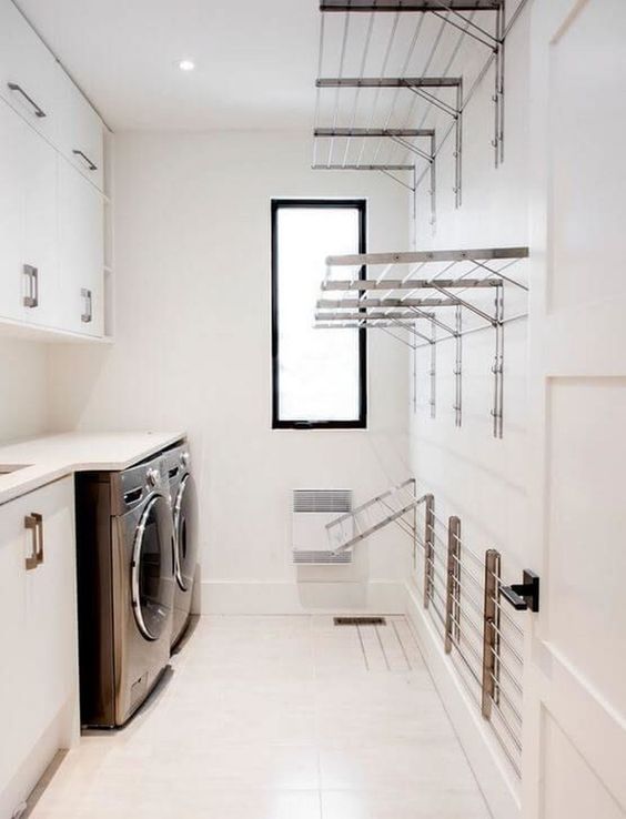 a neutral laundry with sleke cabinets, a white countertop, lots of holders for clothes and clothes hangers and a small window