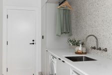 a neutral laundry with terrazzo tiles and a floor, sleek white cabinets, clothes hangers and a washing machine and a dryer is a very stylish and clean space