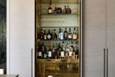 a refined built-in home bar with glass shelves and sleek gold drawers for storage is super chic
