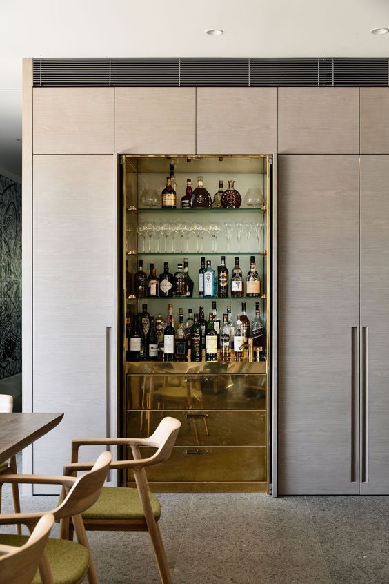 a refined built-in home bar with glass shelves and sleek gold drawers for storage is super chic
