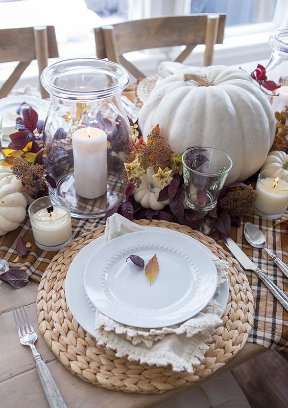 a rustic fall centerpiece of candles, white pumpkins, leaves and foliage is bright and cool