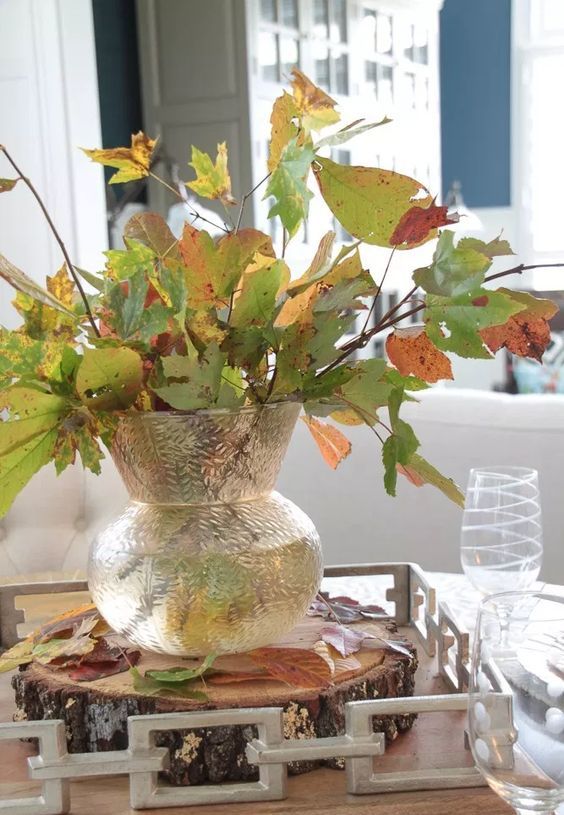 a simple and all-natural fall centerpiece of a clear vase with fall leaves put on a wooden slice