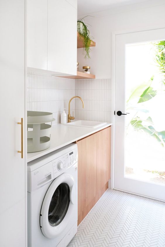 a small and chic contemporary laundry with white and stained cabinets, a white chevron tile floor, a washing machine and some open shelving