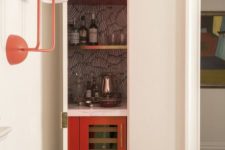 a small hidden bar with a wallpaper backsplash, open gold shelves and a fridge is chic and cool