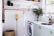a small modern laundry with open shelves, grey shaker style cabinets, stone countertops, a washing machine and a round sink, brass fixtures