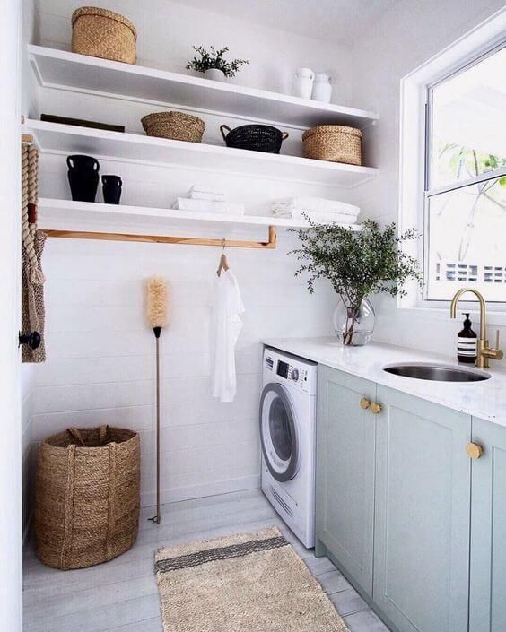 a small modern laundry with open shelves, grey shaker style cabinets, stone countertops, a washing machine and a round sink, brass fixtures