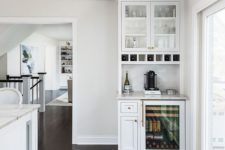 a small white home bar with open and closed storage compartments, a tile backsplash and a fridge for bottles
