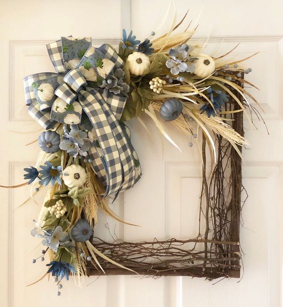 a square wreath with sticks and twigs, a plaid box, blue and white pumpkins, greenery, wheat and feathers