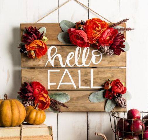 a stained wooden plaque sign decorated with bright faux blooms, greenery and even pinecones