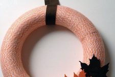 a stylish yarn fall wreath with orange yarn, colorful fabric leaves and a dark ribbon is a cool decoration