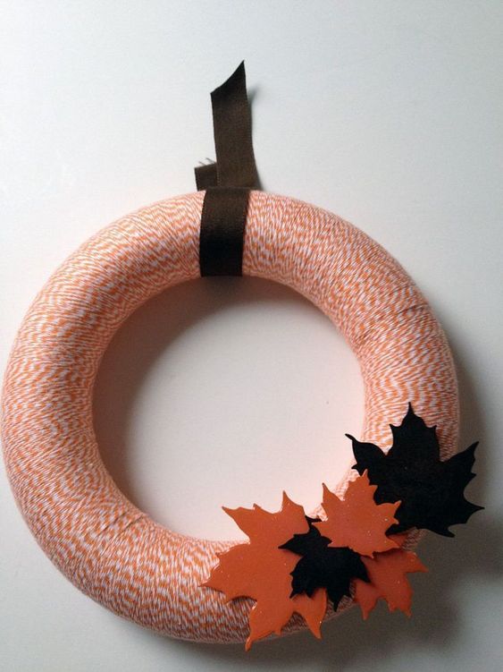 a stylish yarn fall wreath with orange yarn, colorful fabric leaves and a dark ribbon is a cool decoration