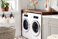 a welcoming laundry with an open shelf, dove grey cabinets, stone countertops, a stained console with a washing machine and a dryer, potted greenery