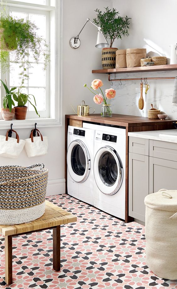 a welcoming laundry with an open shelf, dove grey cabinets, stone countertops, a stained console with a washing machine and a dryer, potted greenery