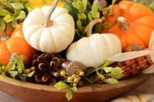 a wooden bowl with greenery, berries, pumpkins and pinecones is a bright and natural autumn centerpiece or decoration