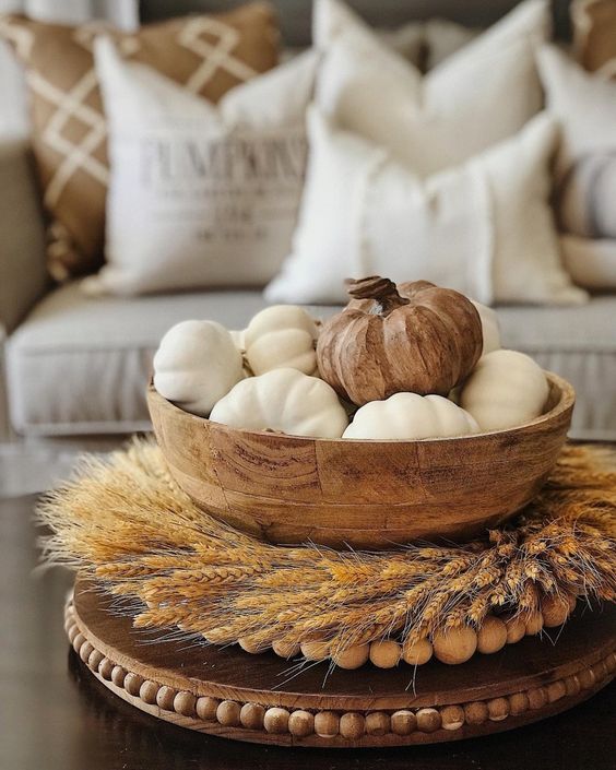 a wooden bowl with white faux pumpkins and a wooden one on top, a wheat wreath and wooden beads for a farmhouse space