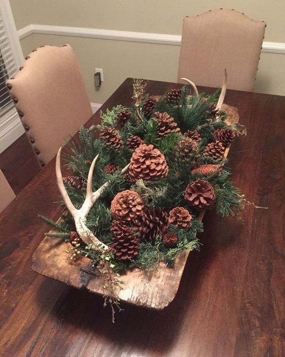 a woodland fall centerpiece of a dough bowl with evergreens, pinecones of various kinds and antlers for autumn