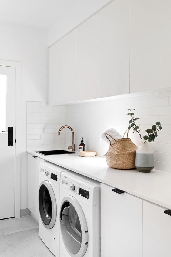 an edgy white laundry with sleek cabinets, black handles, a basket for storage, white appliances and built-in lights