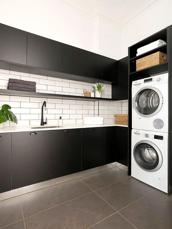 an elegant monochromatic laundry with matte black cabinets, white subway tiles on the backsplash, white appliances and baskets for storage