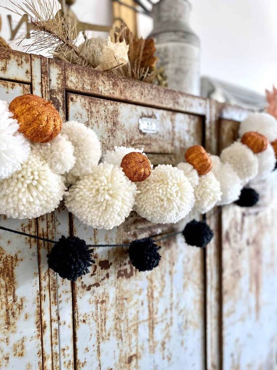 pretty fall garlands of pompoms, black and white ones of yarn and small orange pumpkins are amazing for fall and Thanksgiving decor