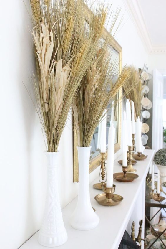 tall white vases with wheat and corn husks and tall and thin candles in candle holders for decorating the mantel