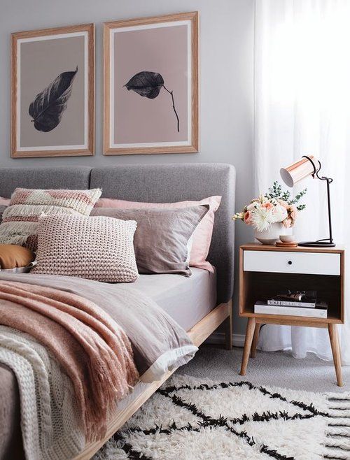 a Scandinavian bedroom with a grey upholstered bed, pink and grey bedding, a pink and grey gallery wall and a printed rug