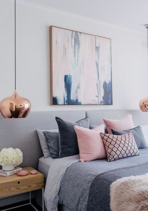 a Scandinavian bedroom with a grey upholstered bed with grey and pink bedding, stainted nightstands and copper pendant lamps