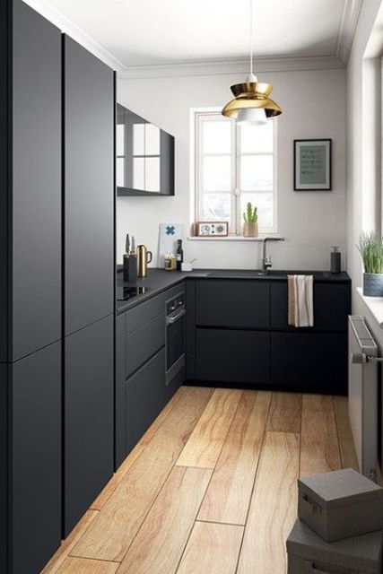 a Scandinavian kitchen with white walls, matte black cabinets and built-in appliances, a gold pendant lamp and accessories