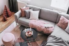 a Scandinavian living room with dove grey walls, a grey sofa and pink and grey pillows, a black coffee table and a pink pouf, a geo grey, beige and pink rug