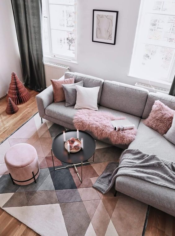 a Scandinavian living room with dove grey walls, a grey sofa and pink and grey pillows, a black coffee table and a pink pouf, a geo grey, beige and pink rug