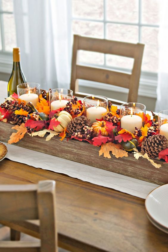 a beautiful Thanksgiving centerpiece of fake fall leaves, pinecones, berries, corn and candles in clear candle holders