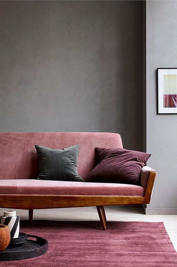 a beautiful and refined living room with grey walls, a pink sofa with jewel tone pillows, a pink rug