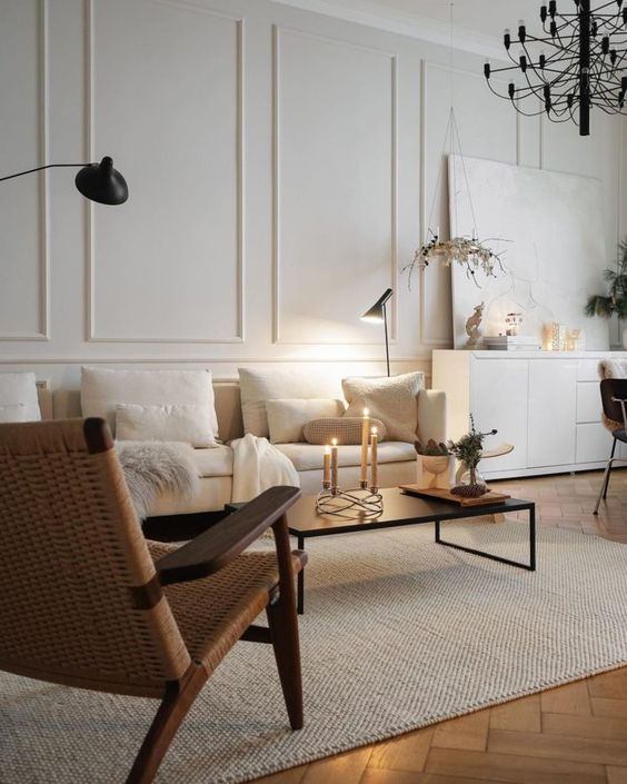 a beautiful contemporary living room with molding on the walls, a white sofa, a black coffee table, a woven chair, a black chandelier and an artwork