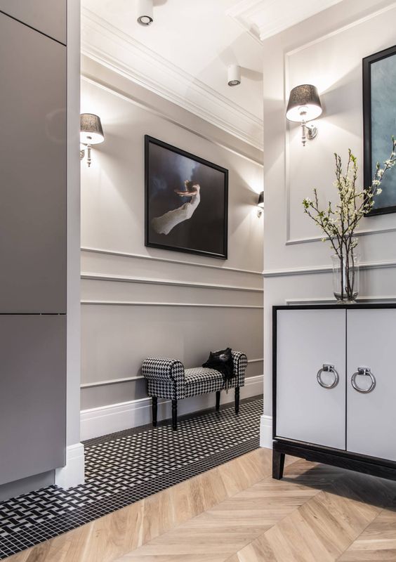 a beautiful entryway with molding on the walls, printed floor and a mini bench, a storage unit with ring pulls and a bold artwork