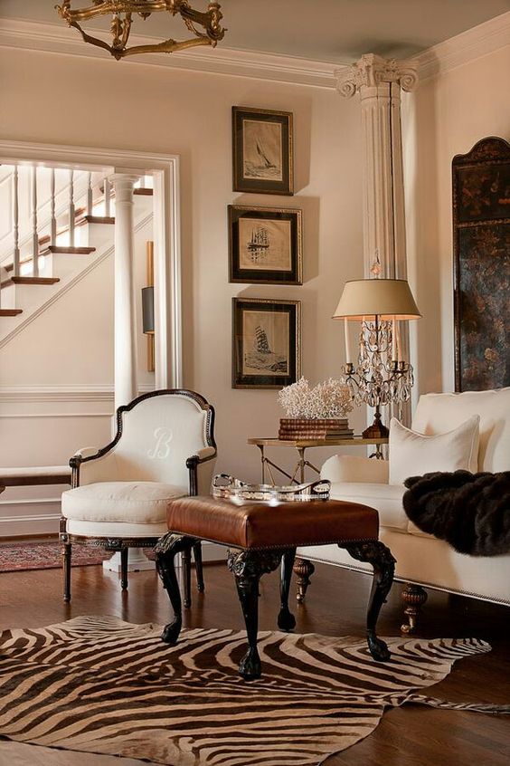 a beautiful vintage-infused living room with a neutral sofa, an antique white chair, a leather ottoman, a zebra print rug and a grid gallery wall