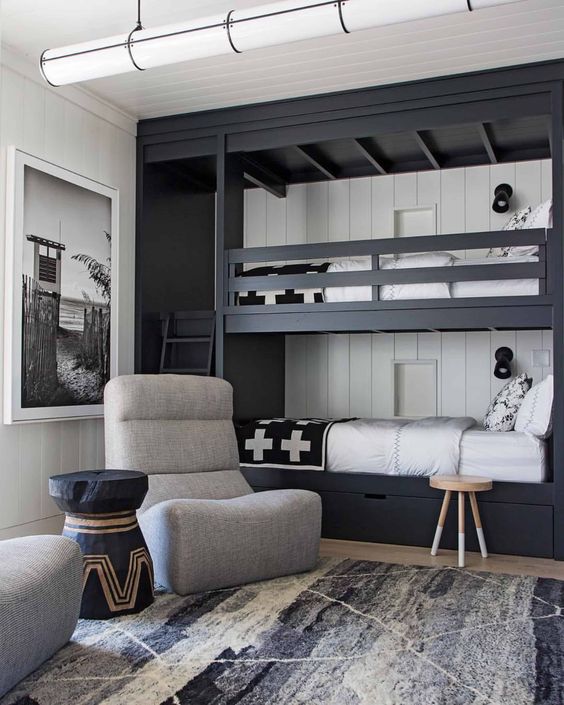 a black and white kids' room with a black built-in bunk bed, with black and white bedding, grey chairs and a black coffee table