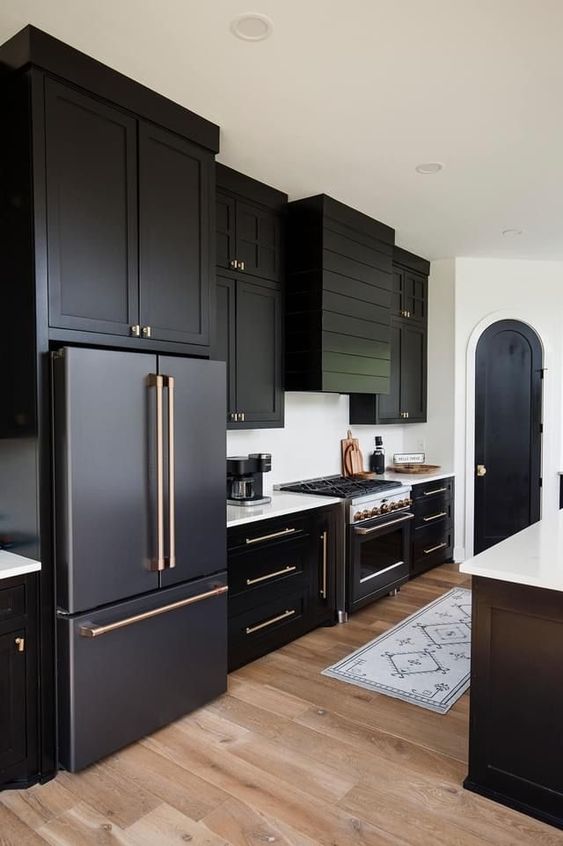a black farmhouse kitchen with shaker cabinets, a shiplamp hood, white countertops, gold handles and a black and white kitchen island
