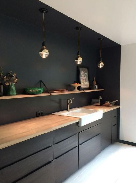 a black kitchen with light-colored wood countertops, pendant lamps and open shelving over the cabinets