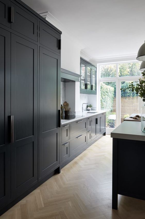 a black kitchen with shaker cabinets, white countertops and a backsplash plus a glazed wall to maximize natural light