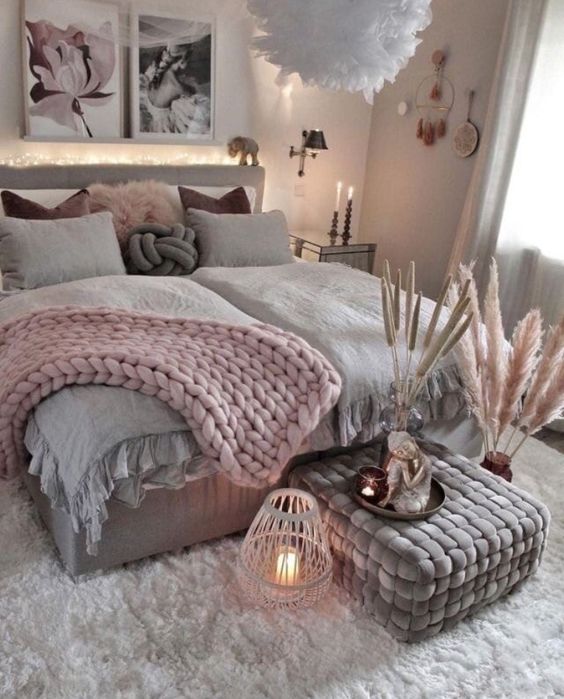 a boho Scandi bedroom with grey walls, a grey bed with pink and grey bedding, a grey pouf, a white rug, pampas grass and candles